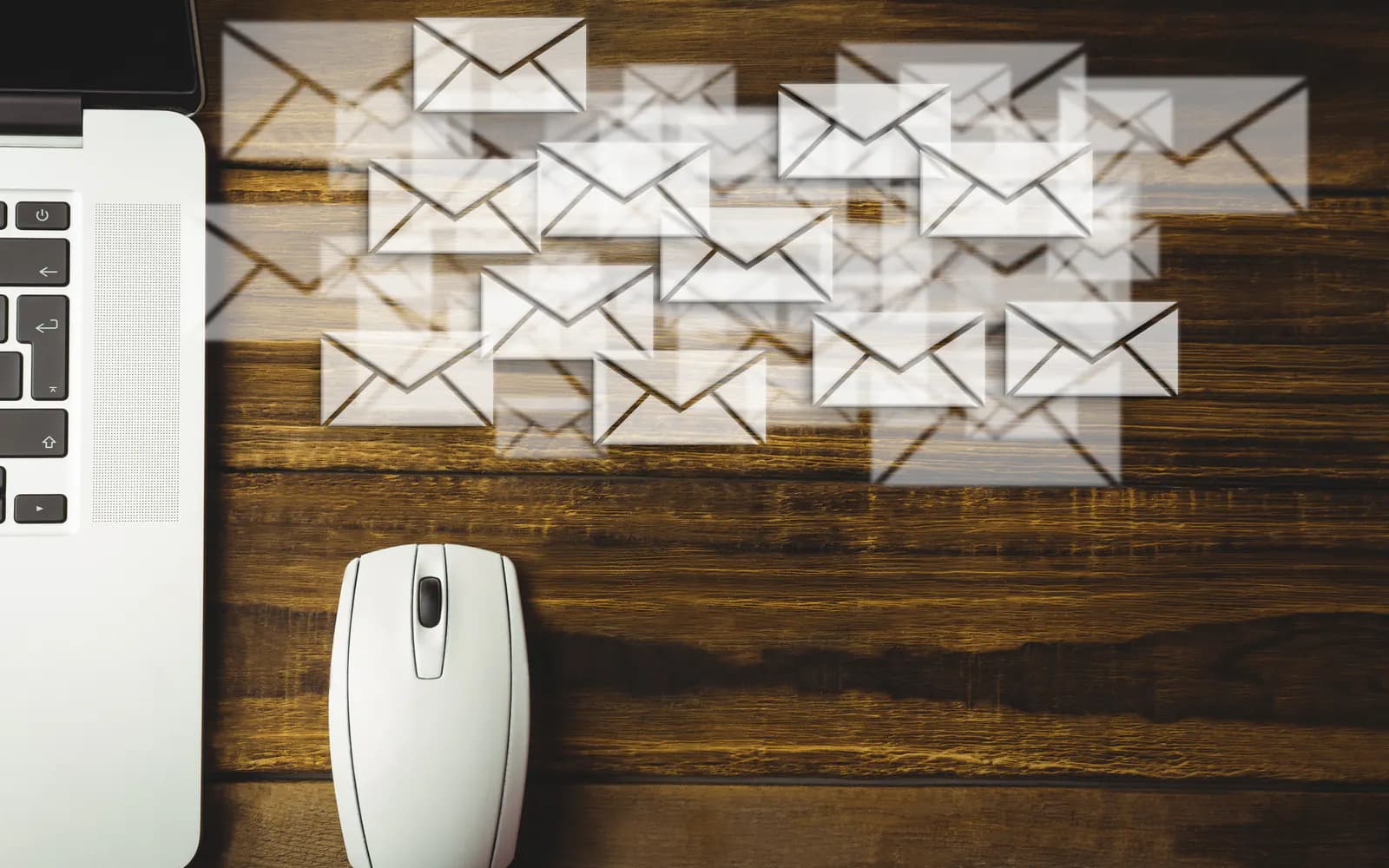 Dozens of email envelopes flying out of a laptop on a wooden desk